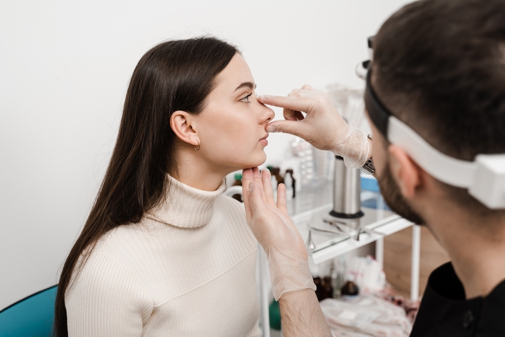 Female doctor gently examines a patient's nose during a revision rhinoplasty consultation at Natural Clinic